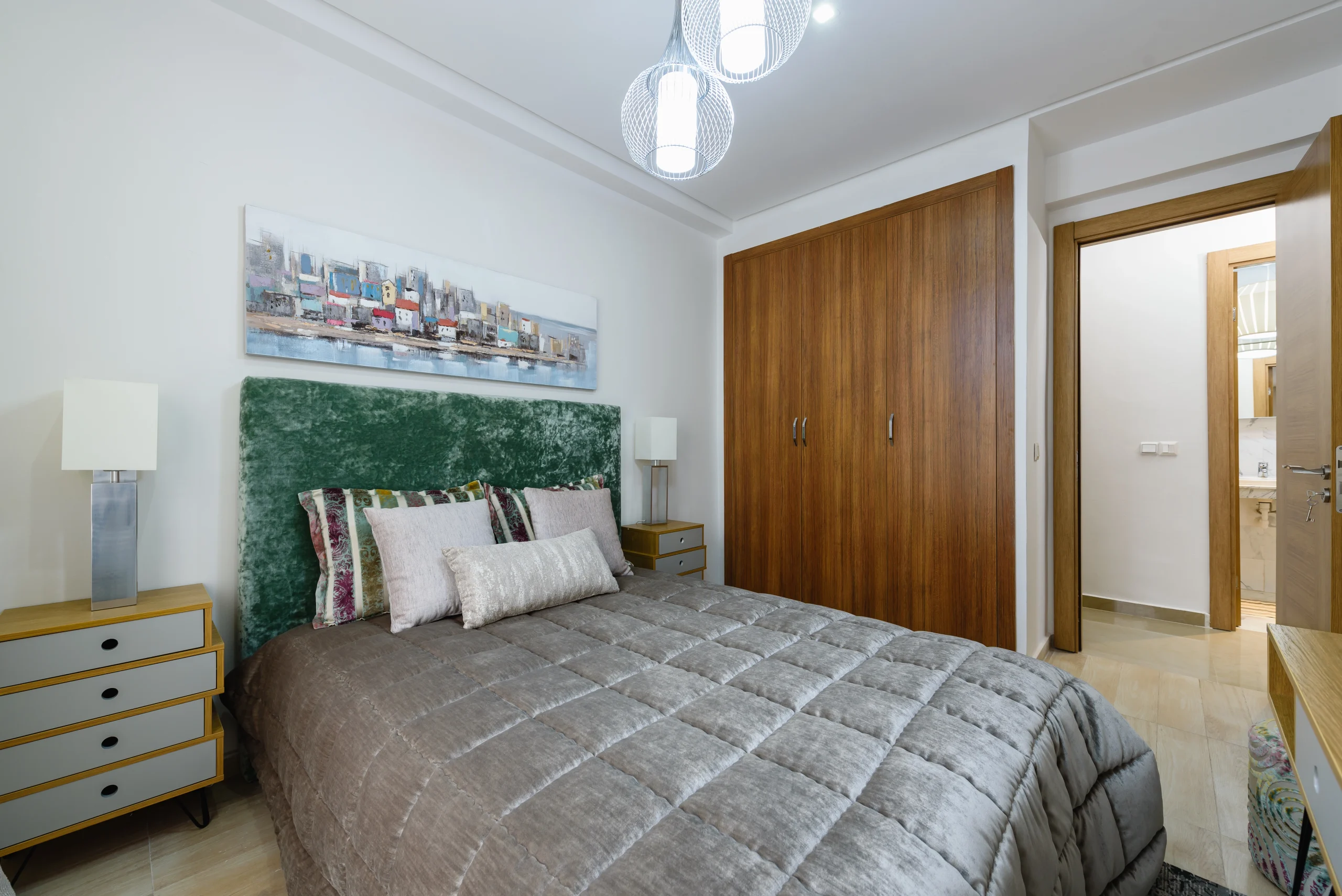Chambre élégante d'un appartement à Oujda avec tête de lit verte, grand placard en bois et luminaire design.