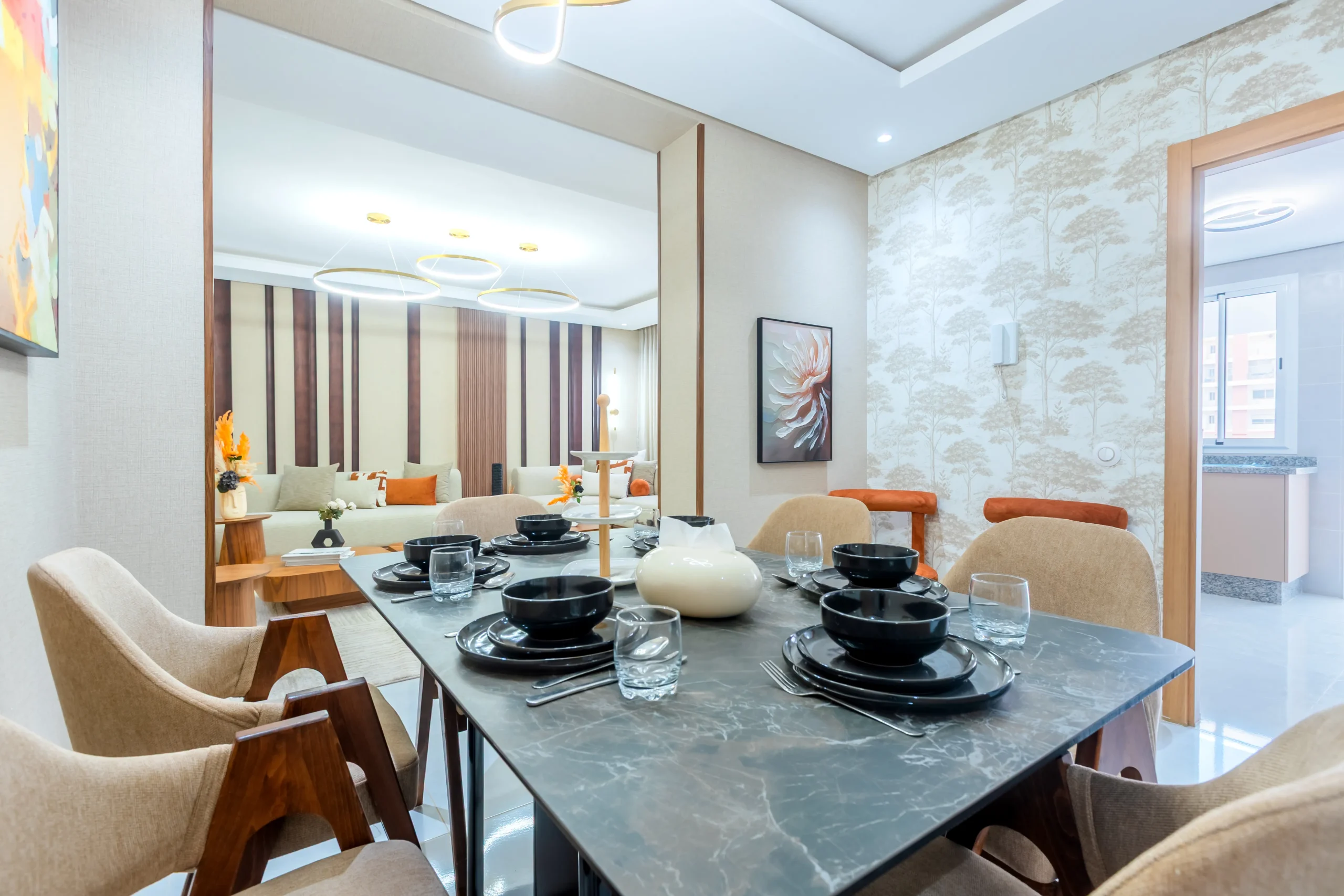 Salle à manger moderne avec table en marbre, vaisselle noire et salon chaleureux en arrière-plan