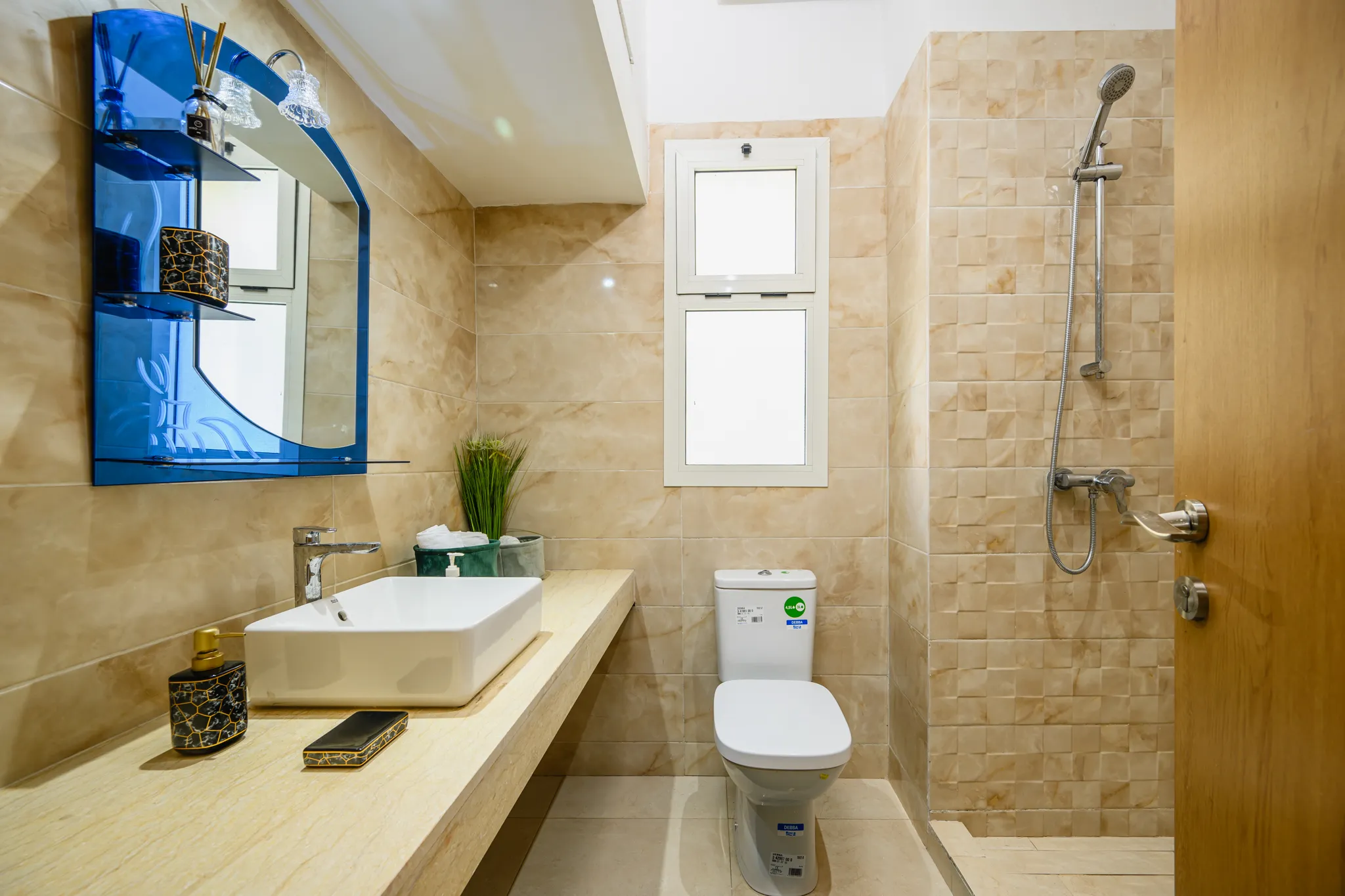Salle d'eau avec vasque rectangulaire, miroir design bleu et douche à l'italienne aux finitions beiges.