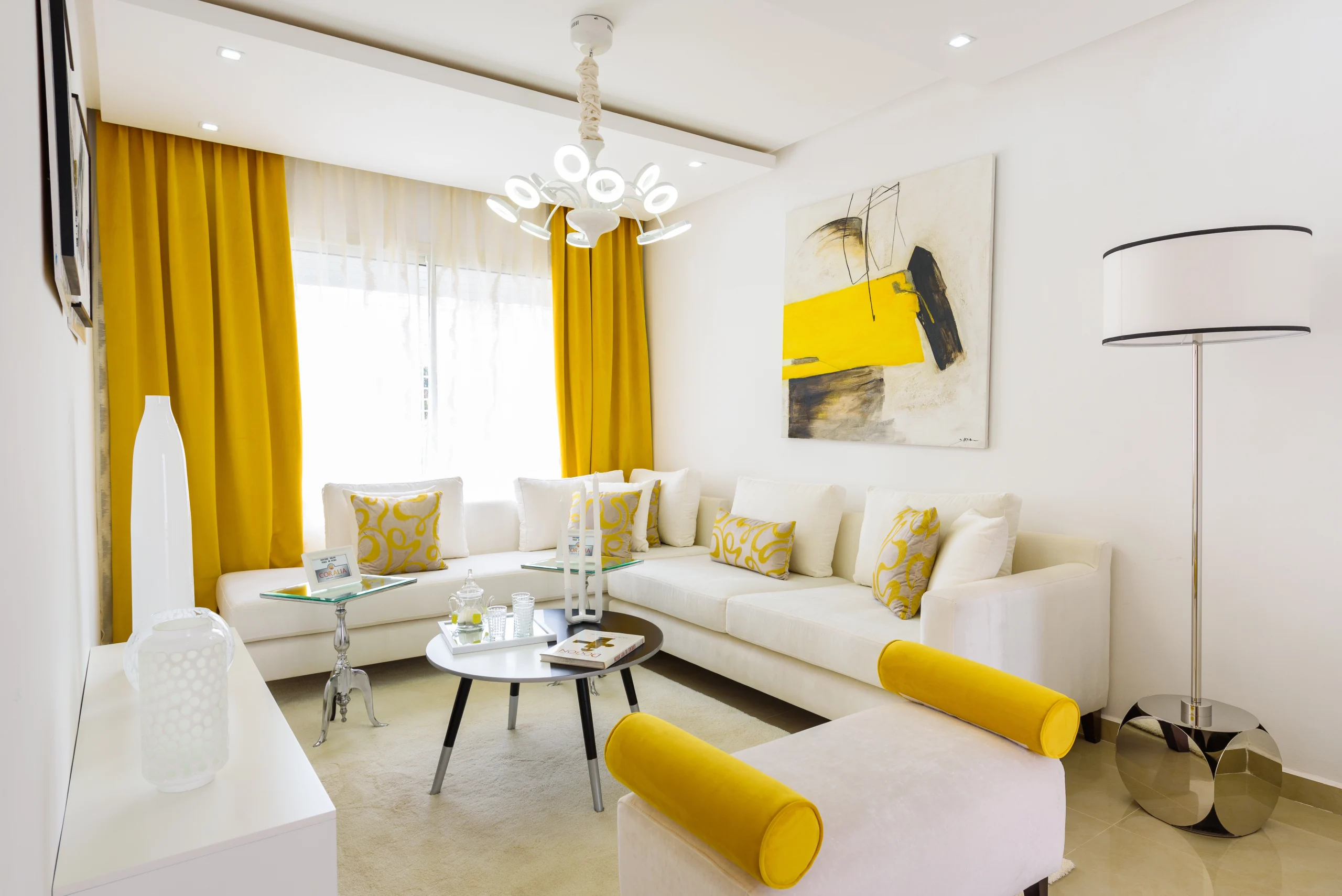 Salon lumineux d'un appartement à Oujda avec canapé d'angle blanc et rideaux jaunes modernes.